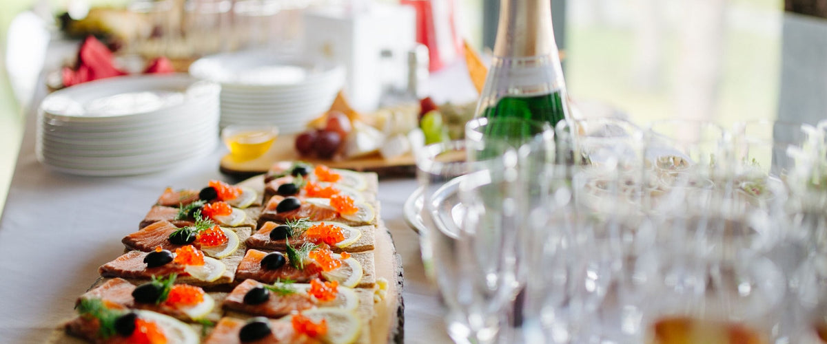 Aperitive: Häppchen-Buffet mit Lachs-Kanapees, Sektflasche und bereitstehenden Gläsern im hellen Tageslicht