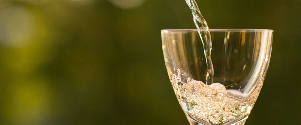 Chenin Blanc: Weißwein wird ins Glas gegossen, grünes Bokeh
