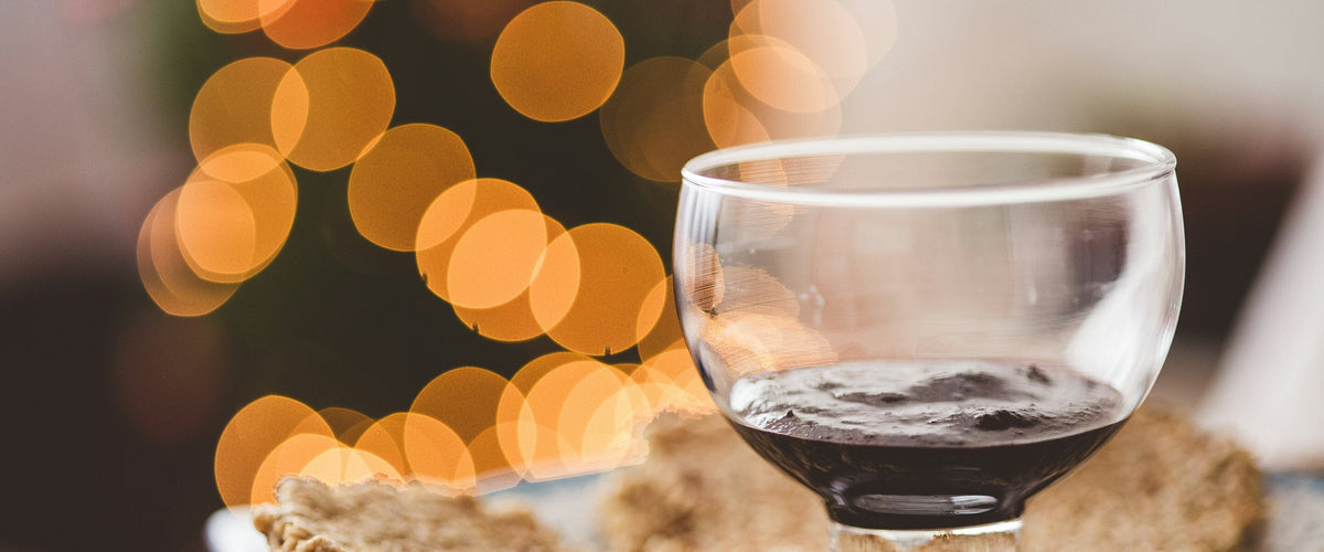 Dessertweine: Dessert-Schälchen mit dunklem Süßwein auf Gebäck, warmes Lichterbokeh im Hintergrund