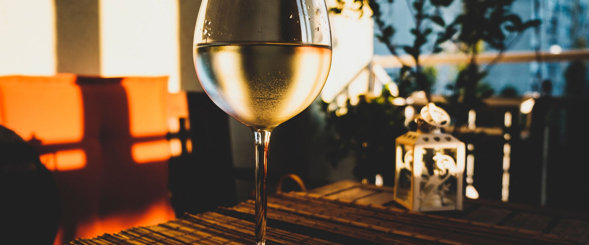 Feinherb: Glas Weißwein auf Holztisch auf der Terrasse im warmen Abendlicht, Laterne daneben