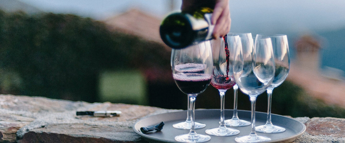 Weine aus Languedoc-Roussillon: Rotwein wird auf einer Steinmauer eingeschenkt, Mittelmeerhügel und Dächer dahinter