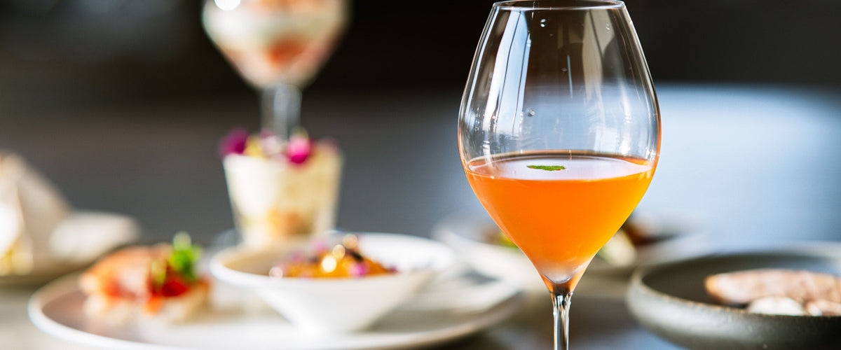 Süß: Stielglas mit goldorangefarbenem Dessertwein vor Desserts in Schalen und Gläsern