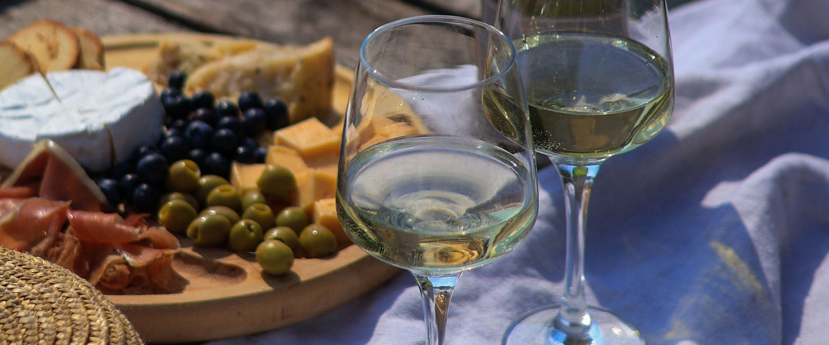 Wein zur Käseplatte: Picknick am Wasser mit Camembert, Trauben und zwei Gläsern Weißwein