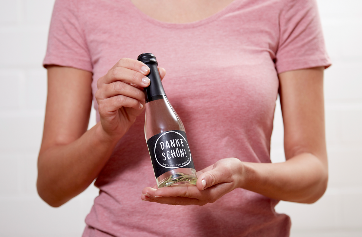 Frau hält eine Piccolo-Flasche Perlwein Dankeschön von Vom Feinsten in den Händen