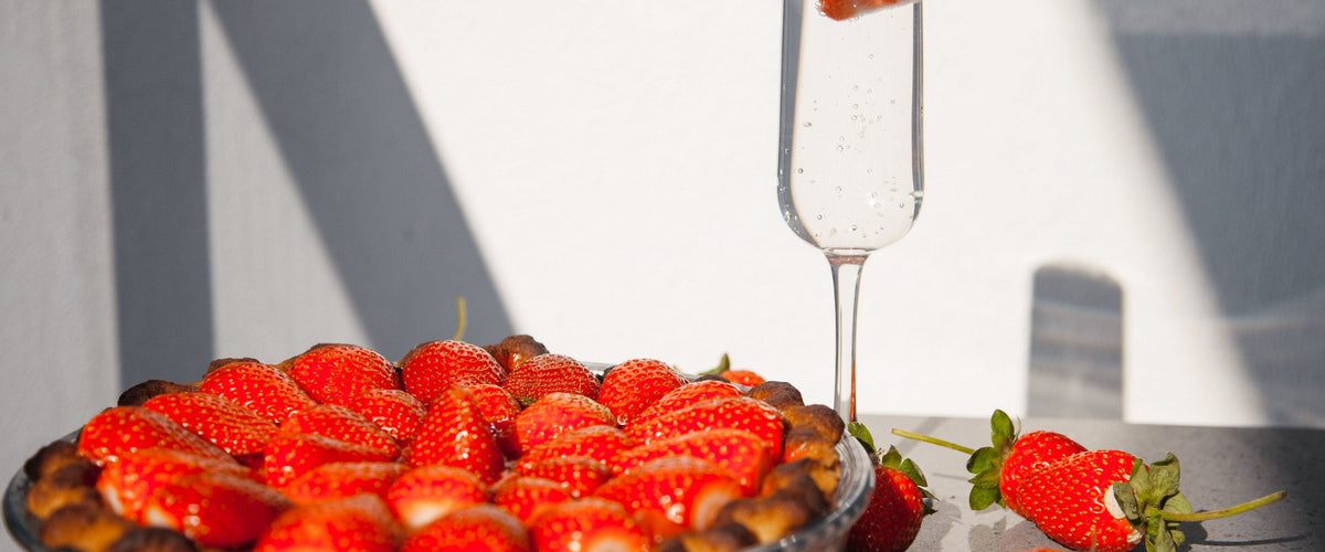 Fruchtsecco: Erdbeertarte, daneben eine Sektflöte mit Erdbeere darin, helles Licht
