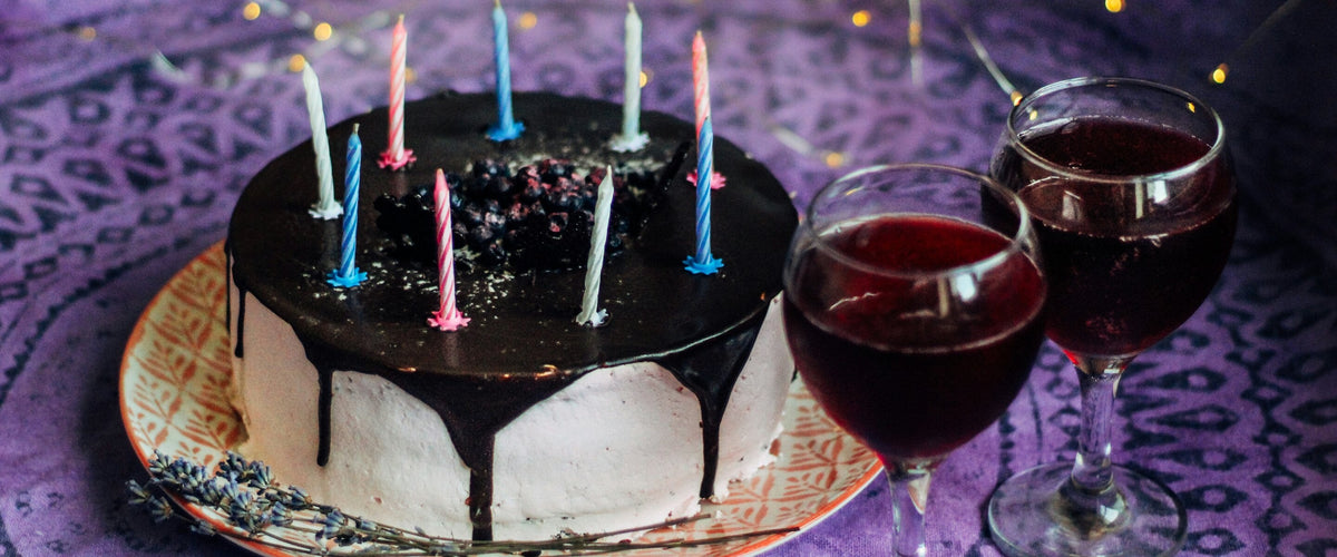 Geburtstag: Schokotorte mit Kerzen und zwei Rotweingläsern, lila Tuch