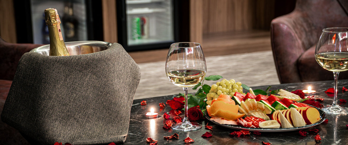 Halbtrocken: Niedriger Tisch mit Obstplatte, Teelichtern und Rosenblättern, zwei Gläser Weißwein, Sekt im Kühler