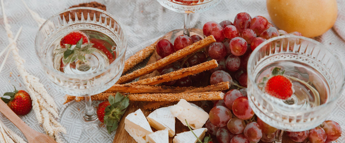 Lieblich: Von oben: Kristallschalen mit hellem Wein und Erdbeeren, dazu Trauben, Käse und Grissini auf Leinentuch