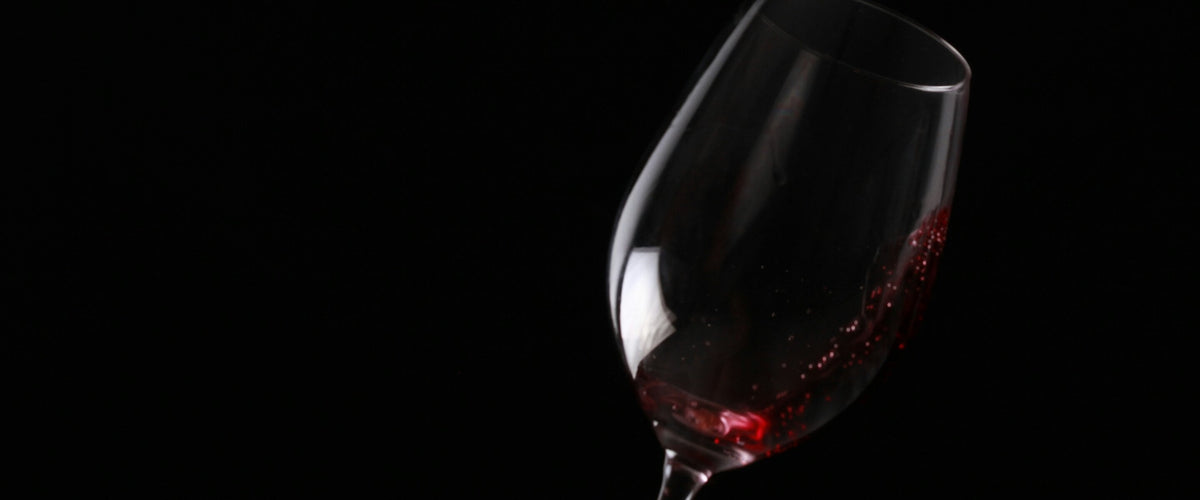 Merlot: Rotweinglas vor Schwarz, Hand unten abgeschnitten