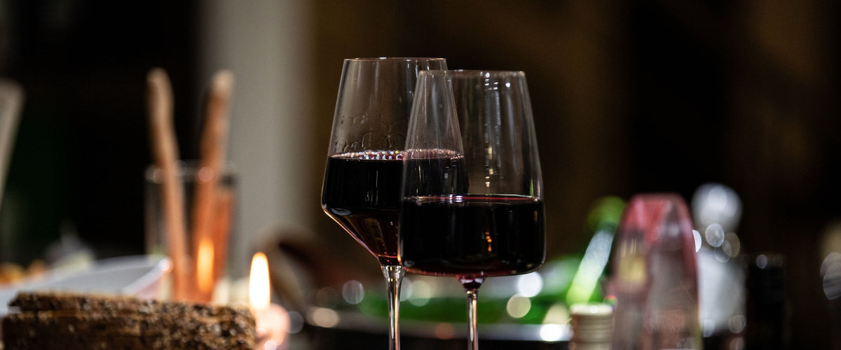 Rotwein: Zwei Gläser Rotwein am festlich gedeckten Tisch, Kerze im Hintergrund