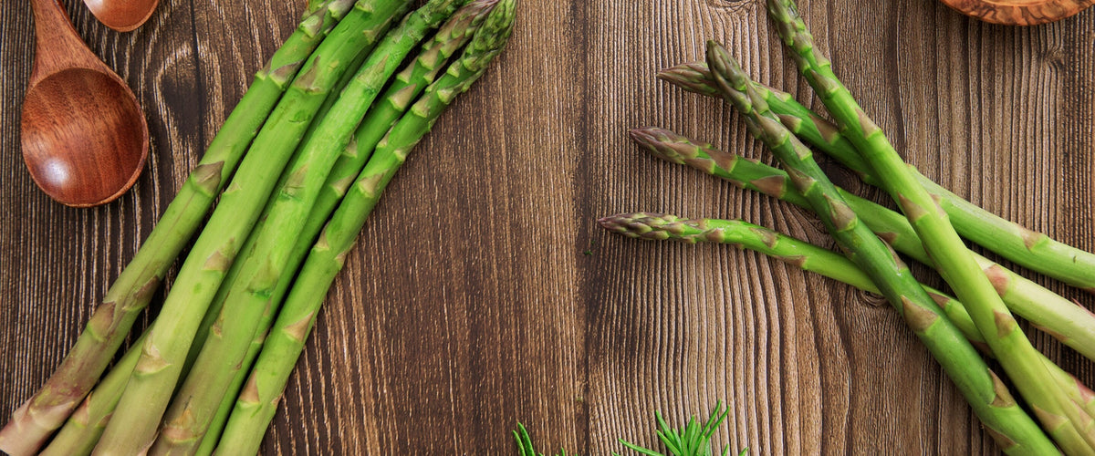 Wein zu Spargel: Grüner Spargel, Rosmarin und Holzlöffel auf dunklem Holztisch, von oben