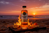Flasche Cocktail Whiskey Sour von Punch Club auf einem Holzbrett am Strand bei Sonnenuntergang, daneben Orangenscheiben