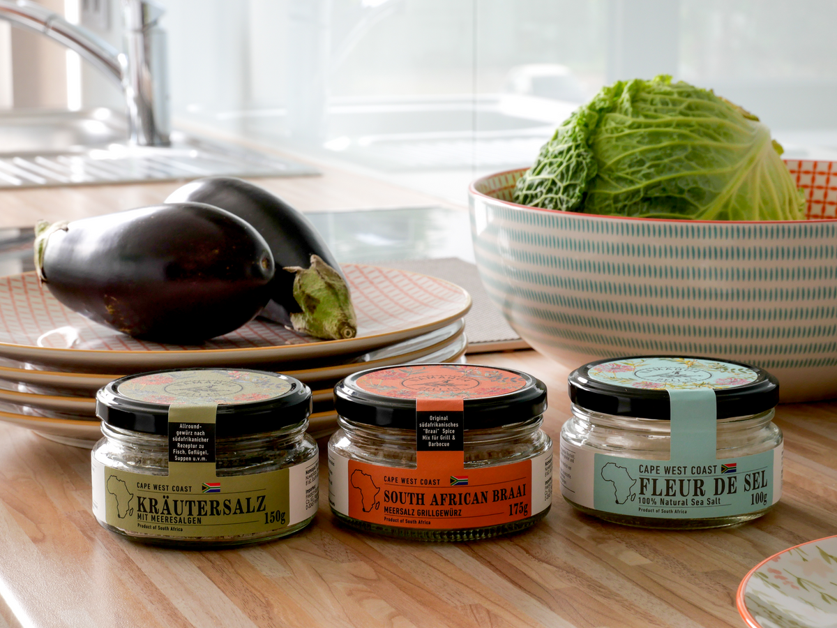 Drei Gläser Cape West Coast Salz, darunter Fleur de Sel, mit Aubergine und Wirsing in einer Küche