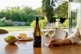 Flasche Kleine Zalze Vineyard Selection Chardonnay mit zwei Gläsern und Trauben auf einem Tisch mit Blick in den Garten