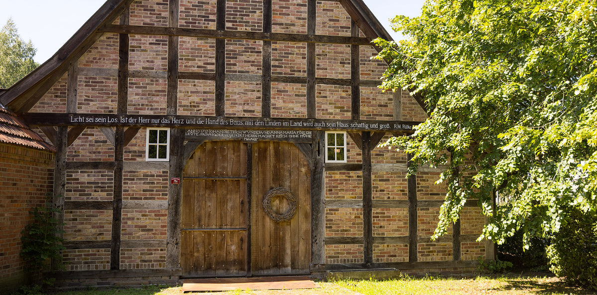 Fachwerk-Hofgebäude der Familie Lütvogt in Wagenfeld mit großem Holztor, daneben ein alter Baum