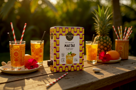 Punch Club Mai Tai 1,5-L-Box mit Gläsern, Ananas und Strohhalmen auf einem Tisch im Garten
