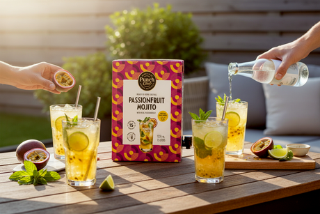 Punch Club Passionsfrucht Mojito 1,5-L-Box mit eingeschenkten Gläsern, Limette und Minze auf einer Terrasse