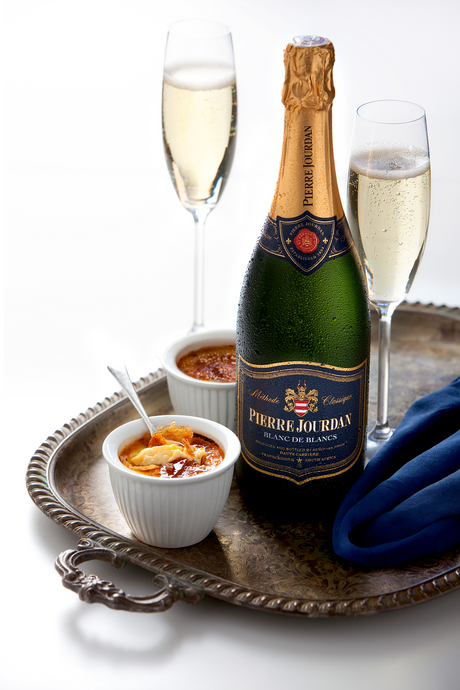 Flasche Pierre Jourdan Blanc de Blancs mit zwei Sektgläsern und Crème brûlée auf einem Silbertablett