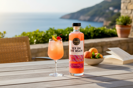 Flasche Punch Club Sex on the Beach mit eingeschenktem Cocktail auf einem Holztisch am Meer