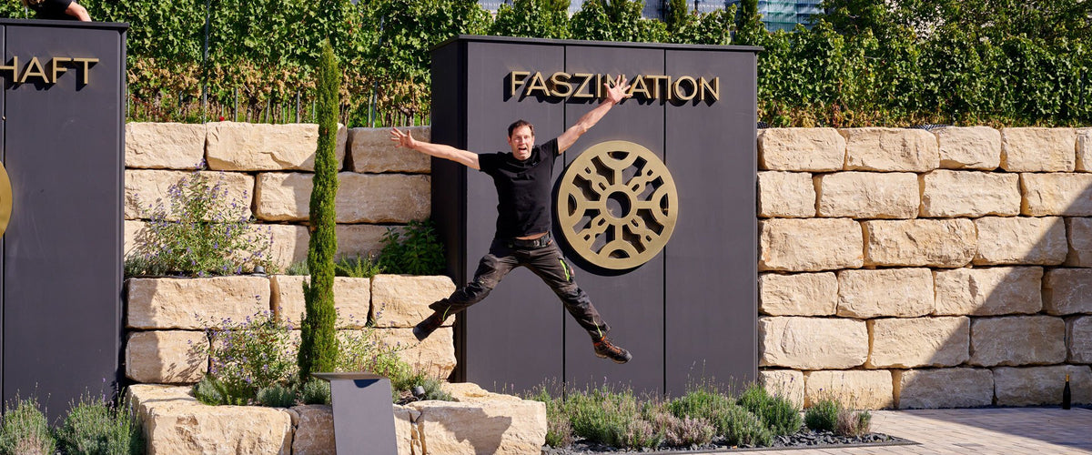 Eric Manz springt vor der Stele mit dem Wort Faszination und der goldenen Rosette in die Luft