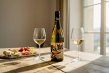 Flasche What the Duck Colombard Sauvignon Blanc mit zwei Gläsern Weißwein und Vorspeisen auf einem Tisch
