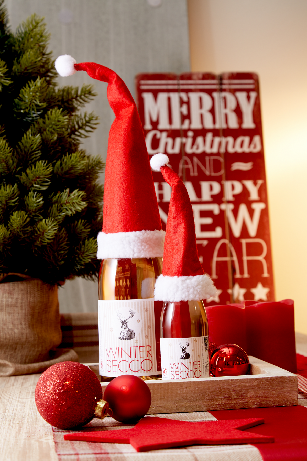 Wintersecco mit Zimt und Nelke von Vom Feinsten als Flasche und Piccolo mit Weihnachtsmützen vor einem Merry-Christmas-Schild