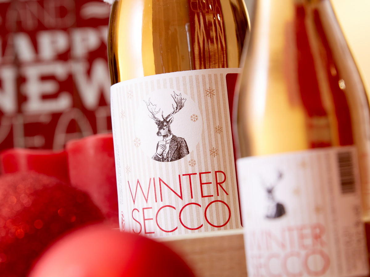 Wintersecco mit Zimt und Nelke von Vom Feinsten als 0,75-l-Flasche und als Piccolo zwischen roten Christbaumkugeln