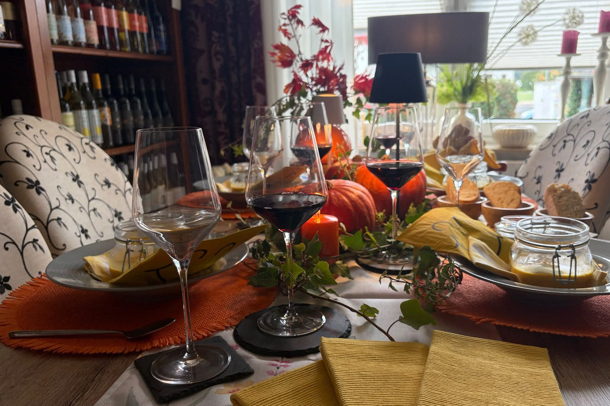 Herbstlich gedeckter Tisch im Weinkontor: Rotwein in Gläsern, Kürbisse, Kürbissuppe und gelbe Servietten, im Hintergrund das Weinregal